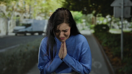 Woman standing on a bustling street wearing a blue sweater outdoors looking distressed and emotional with blurred vehicles in the background creating a tense urban atmosphere.