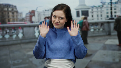 Fototapeta premium Woman standing on city street in casual blue sweater with blurred urban background, capturing a candid moment on a busy day.