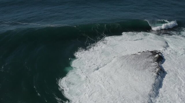 A large ocean wave curls and breaks over an exposed reef, exploding into the air. Captured from high above during a storm swell on the East Coast of Australia.