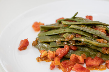 Fried green beans with tomato and onion pieces. Tasty meal with french bean on dinner or lunch on the white plate