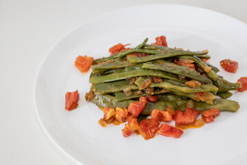 Fried green beans with tomato and onion pieces. Tasty meal with french bean on dinner or lunch on the white plate