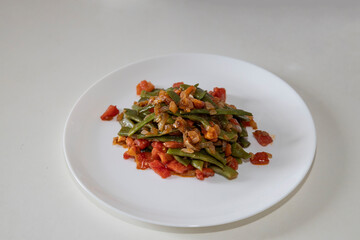Fried green beans with tomato and onion pieces. Tasty meal with french bean on dinner or lunch on the white plate