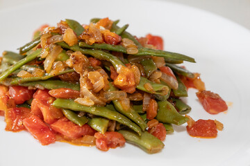 Fried green beans with tomato and onion pieces. Tasty meal with french bean on dinner or lunch on the white plate