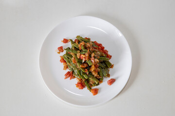 Fried green beans with tomato and onion pieces. Tasty meal with french bean on dinner or lunch on the white plate
