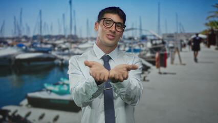 Young man wearing glasses and tie smiles broadly and blows kiss with lips to camera on street pier...