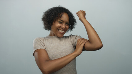 Woman smiling broadly flexes toned arms and raises clenched fists in a bright studio; confidence...