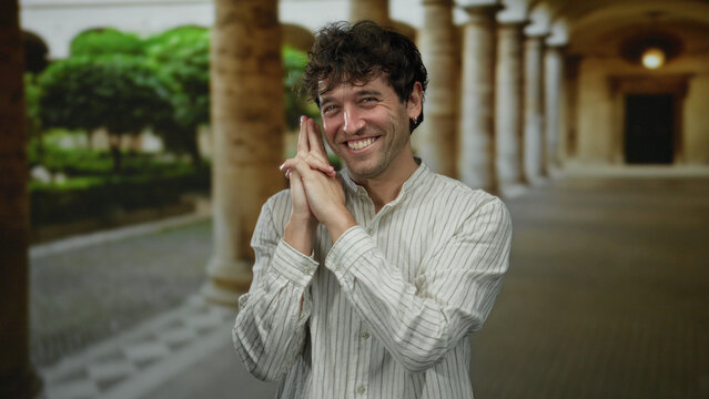 Hispanic man gesturing with hand pistol pose at roman monument with columns in university campus