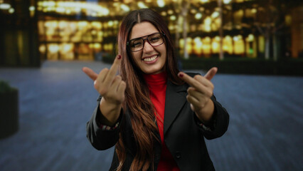 Hispanic woman smiling outdoors makes rude gesture on illuminated city street at night.