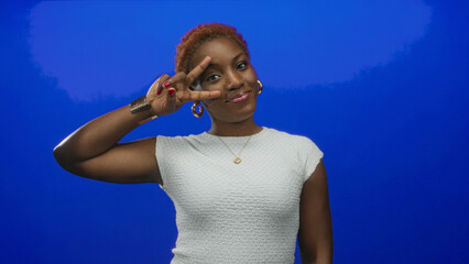 Woman with red manicure and gold hoop earrings holding peace sign with index and middle fingers in studio; serenity.