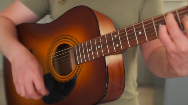 A young artist plays guitar in soft light by the window, caught between inspiration and creative block. His calm surroundings reflect an inner emotional search.