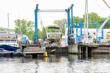 Motorboat hoisted out of the water by a marine lift for routine engine maintenance at a busy marina shot on Toronto Islands in summer