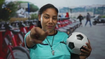 Referee woman wearing turquoise jersey holding soccer ball at bike rental on street; confidence community spirit.
