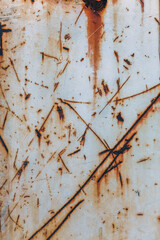 Numerous scratches and marks cover cream colored metal surface rusted from exposure to elements. Weathered intricate textures give a sense of age and industrial wear.