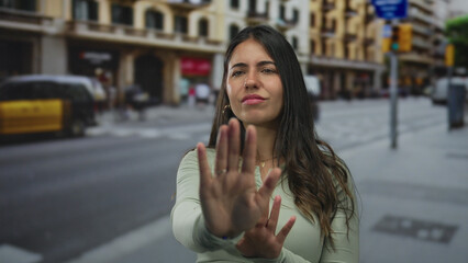 Obraz premium Woman gesturing stop on street with buildings in background, emphasizing urban hustle and outdoor life.