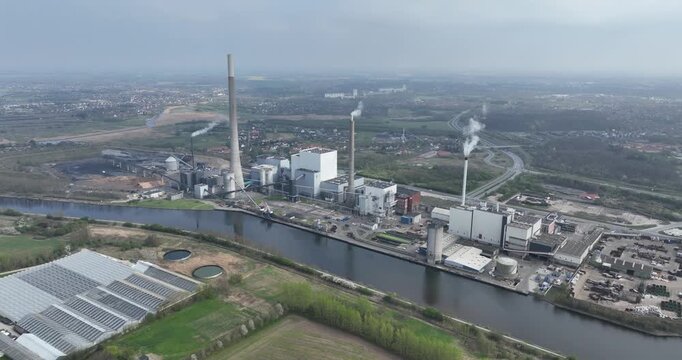 An industrial complex with tall chimneys, a large power plant, and a river flowing beside it