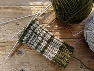 Top view of half done, hand knitted woolen sock and some balls of yarn on a wooden table.