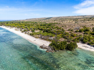 Clear blue sky, vast ocean with beautiful coral, white sand, savanna, and rocky brown hills blend together in the nature of Sumba