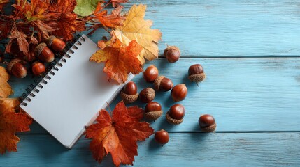 Autumn leaves, acorns, and a blank notepad on a blue wooden background. Use this photo for seasonal promotions, writing, or fall-themed projects.