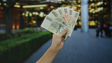 Man holding czech koruna banknotes outdoors in a city setting, showcasing currency in an urban street environment, with blurred background of town life. © Krakenimages.com