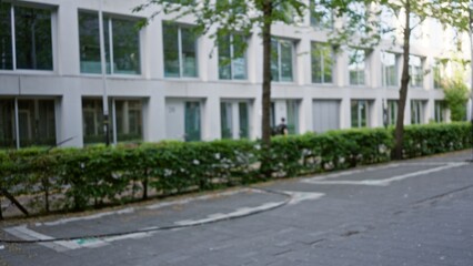 Man walking on a european street with a blurred background featuring modern architecture, greenery, and a subdued urban atmosphere.