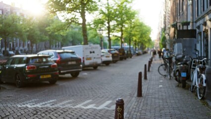 Defocused urban street in a european city with cars, bicycles, and trees lining a sunlit cobblestone road, capturing a peaceful morning scene with a touch of everyday life.