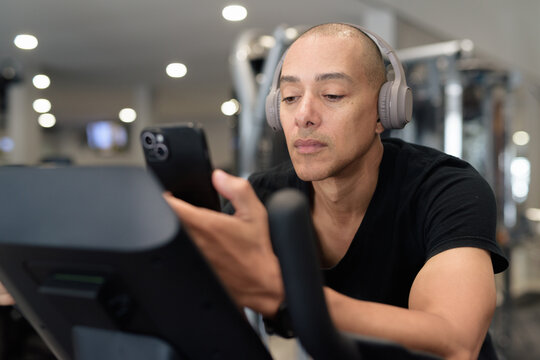 Hispanic bald man athlete doing cardio exercise cycling with bicycle in gym