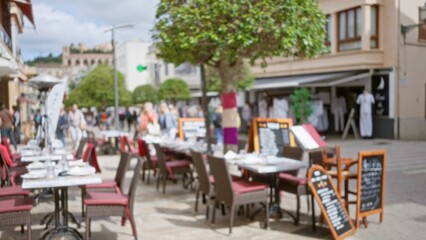 Blurred image of a mediterranean restaurant terrace with tables and chairs, featuring defocused scenery and bokeh effect, capturing a vibrant yet tranquil setting.