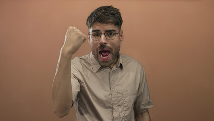 Hispanic man with clenched fist gesture and pursed lips in studio against peach wall; determination.