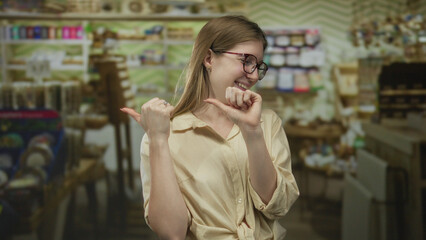 Blonde woman points thumbs to herself inside a brightly lit supermarket aisle lined with colorful product shelves; confidence.