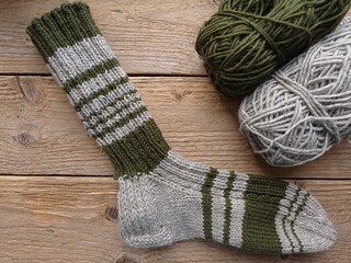 Top view of a hand knitted woolen sock and two balls of yarn on a wooden table.