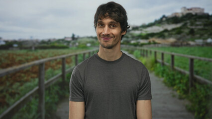 Man smiling showing face on a green park walkway beside a wooden fence and lush foliage; serenity calm contentment.