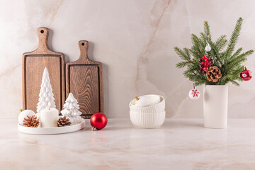 A decorated spruce branches , stylish white candles and Christmas trees on the marble countertop of a modern kitchen. Minimalist style of decorations