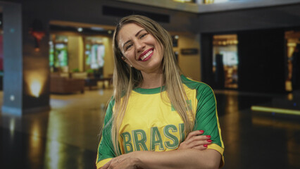 Woman wearing a green and yellow brazil jersey stands with crossed arms in a hotel building; confidence triumph.