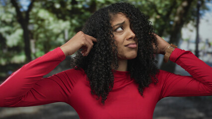 Woman places fingers in ears in dense forest under sunlight filtering through leaves; noise annoyance.