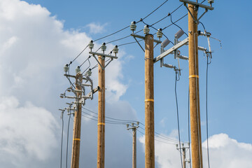 Multiple wooden utility poles with electrical power lines and insulators under partly cloudy sky in rural area for medium voltage electricity distribution and grid infrastructure maintenance