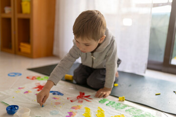 Child painting with fingers on floor at home using colorful tempera colors