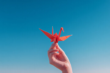 A hand holding an origami crane against a clear blue sky, minimalistic composition with hopeful tone