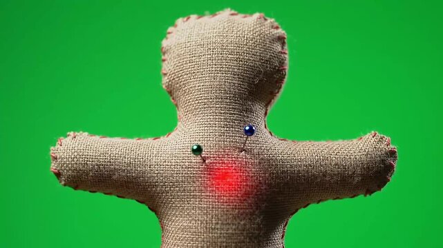 Rear view of a burlap voodoo doll with pins and a red light on a green screen background
