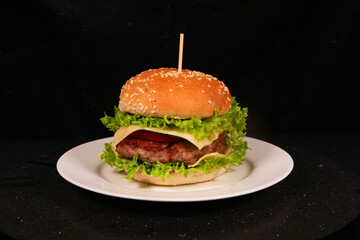 Delicious burger with lettuce, tomato, cheese, and sesame bun on white plate