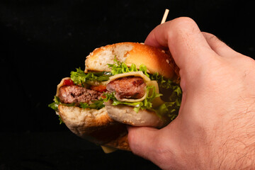 Hand holding a delicious burger with lettuce, tomato, and cheese on a black background