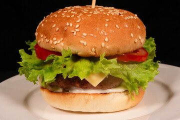 Delicious burger with lettuce, tomato, cheese and sesame bun sitting on white plate