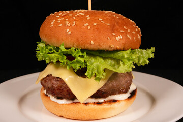 Delicious cheeseburger with lettuce and sesame bun resting on white plate
