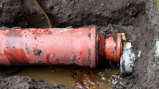 a sewer pipe that has burst, causing a massive leak of waste and excrement. The scene is chaotic, with an orange cable running nearby, highlighting the disastrous failure of the pipe