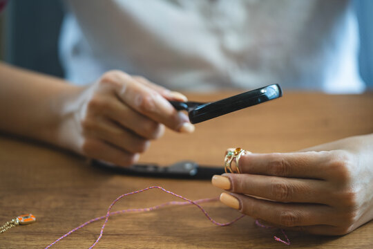 close up on craftswoman hand looks at a ring through a magnifying glass