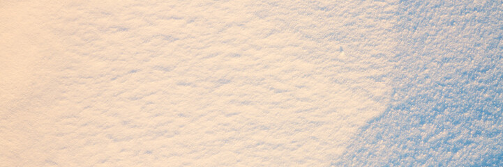 Beautiful winter background with snowy ground. Natural snow texture. Wind sculpted patterns on snow surface. Wide panoramic texture for background and design. Closeup top view with copy space.
