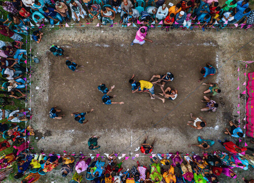 Bogura, Bangladesh - 21 October 2022: Aerial view of a Kabaddi game unfolds on a dusty field, players locked in a vibrant struggle amidst a sea of colorful spectators.