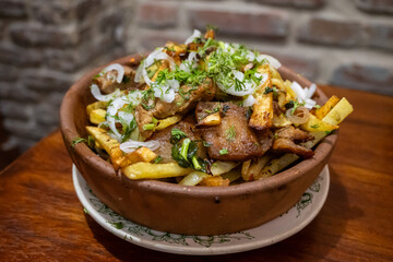Ojakhuri, a Georgian pork and potato dish, is presented in a traditional clay pot, garnished with onions and dill.