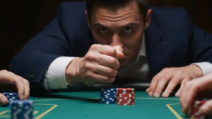 Man in suit at poker table fist clenched stacks of red and blue chips visible