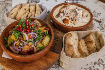 Classic Georgian ojakhuri features roasted potatoes with pork meat, herbs and pomegranate seeds in clay bowl. Creamy shkmeruli contains fried chicken in milky garlic sauce and fresh puri bread
