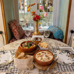 Traditional Georgian dishes on a cozy round table set for two. Food like Shkmeruli chicken in creamy garlic sauce and ojakhuri pork and potatoes are a staple of Georgian cuisine.
